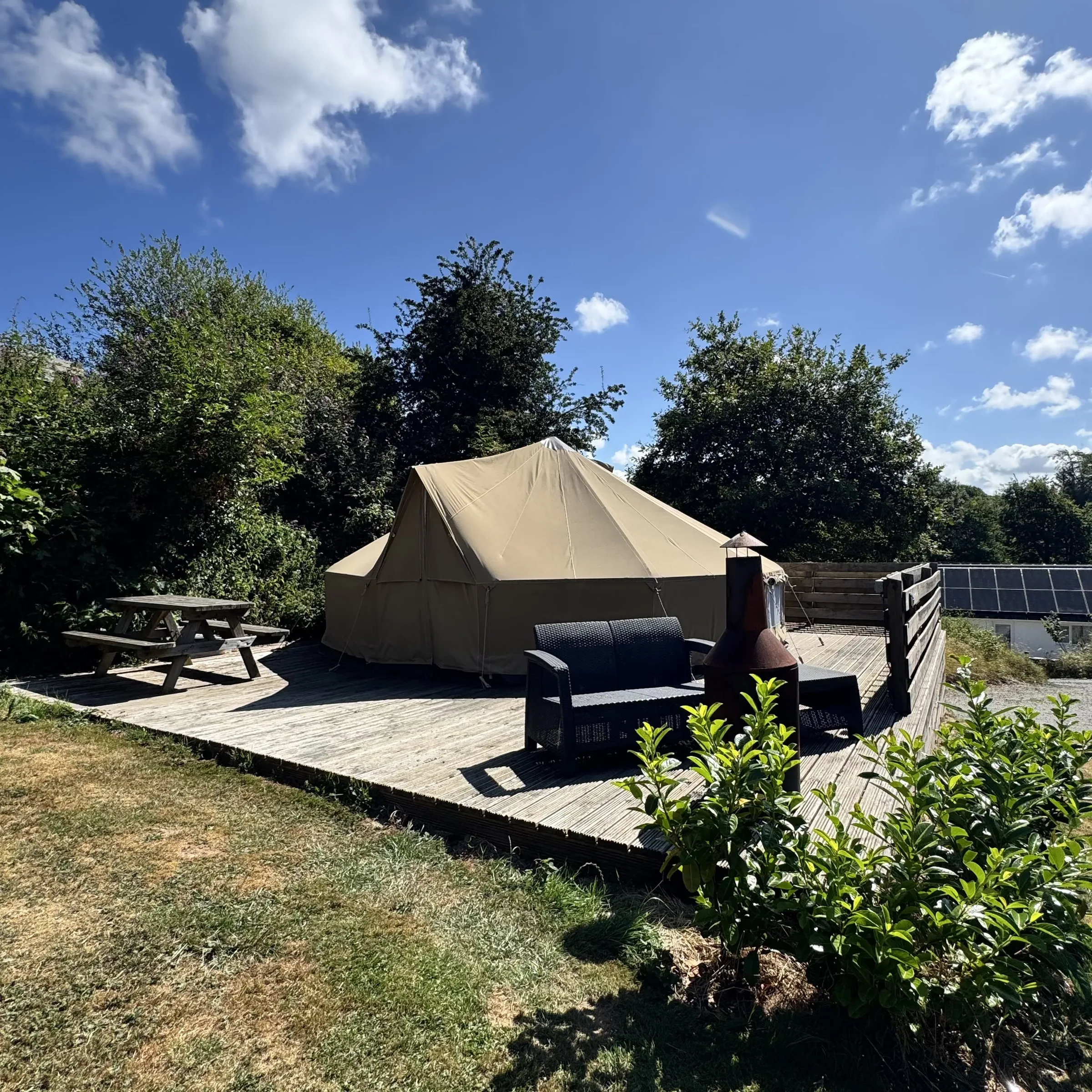 A sand-coloured canvas bell tent on its own timber deck, with a chiminea and a rattan sofa alongside