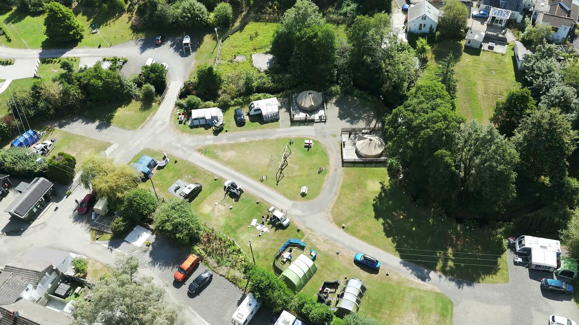 Willow Valley from the air on a bright summer day: the camping field with caravans, awnings and tents on the pitches, two bell tents on their timber decks, the swings on the grass and the lodges among the trees beyond